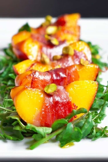 Closeup shot of watercress salad with prosciutto-wrapped peaches.