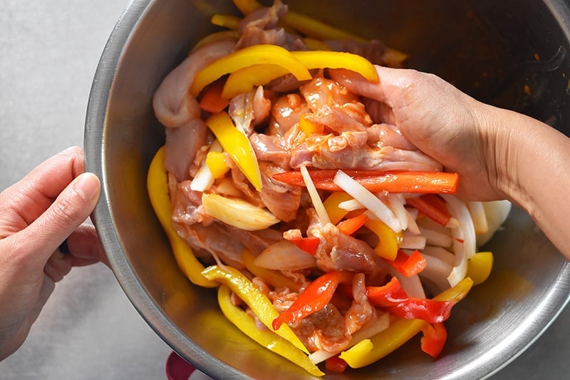 Tossing the chicken and vegetables in the marinade with your hands.
