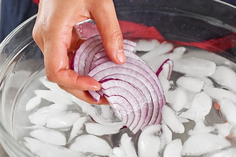 Someone soaking thinly sliced red onions in a bowl of ice water.