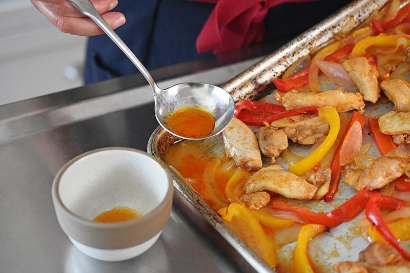 Someone scooping extra liquid from Sheet Pan Chicken Fajitas cooked without a wire rack