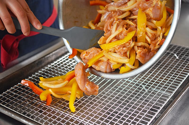 Placing the chicken fajitas and vegetables on a wire rack on top of a rimmed baking sheet