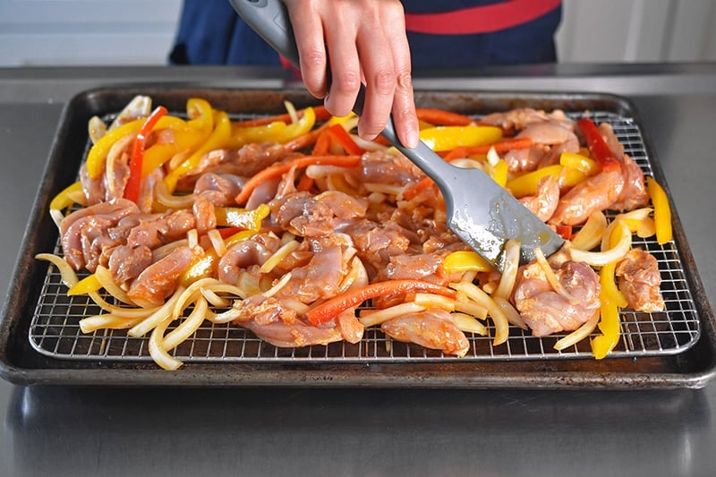 Using a silicone spatula to make the Sheet Pan Chicken Fajitas in a single layer on the wire rack