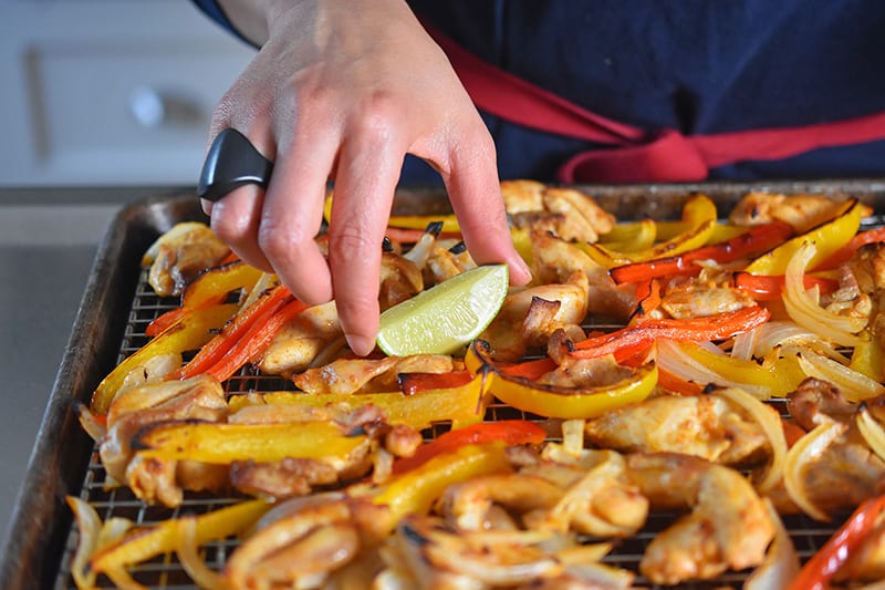 Placing sliced limes on a tray of Sheet Pan Chicken Fajitas 