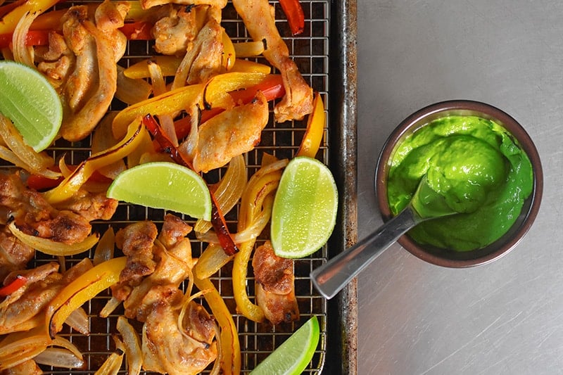 Overhead shot of Sheet Pan Chicken Fajitas and a bowl filled with Avocado Crema 