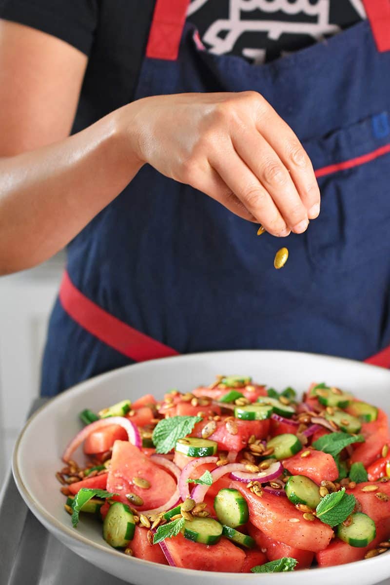 Someone garnishing the paleo and Whole30 Mexican watermelon salad with pepitas.