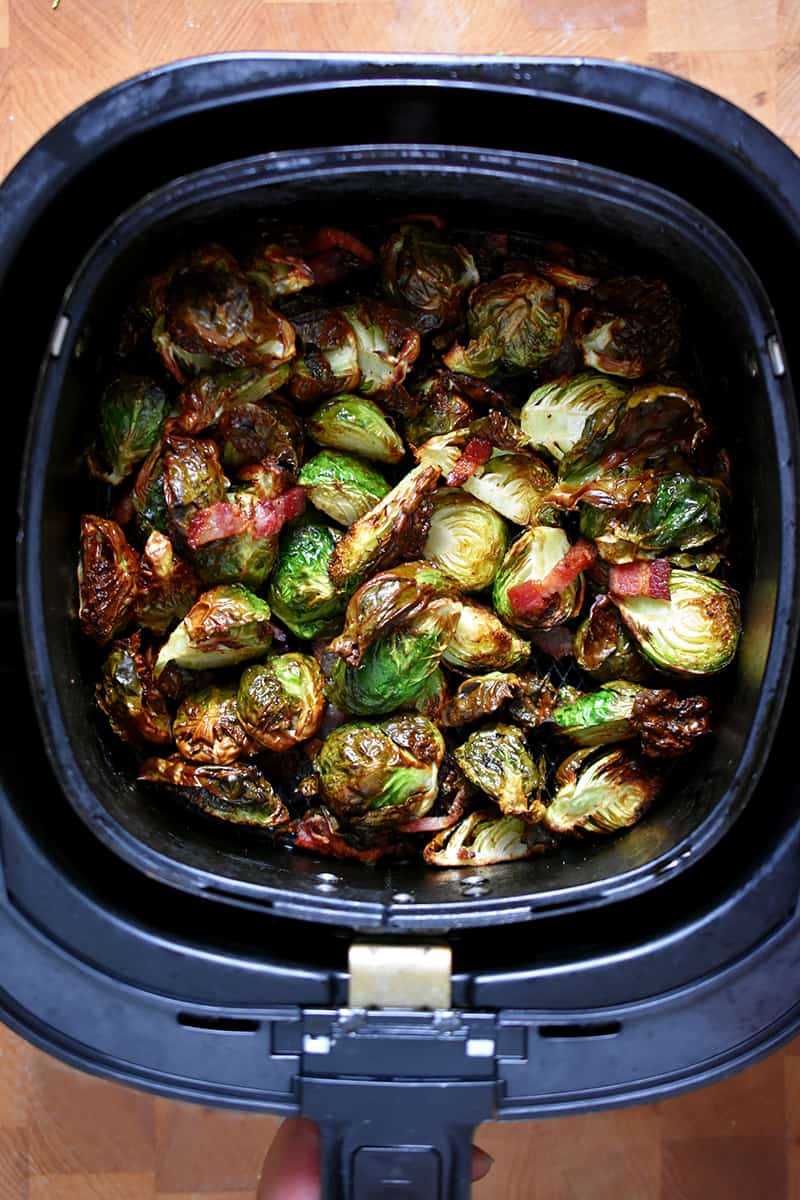 An overhead shot of an air fryer basket filled with golden brown Brussels sprouts with bacon.