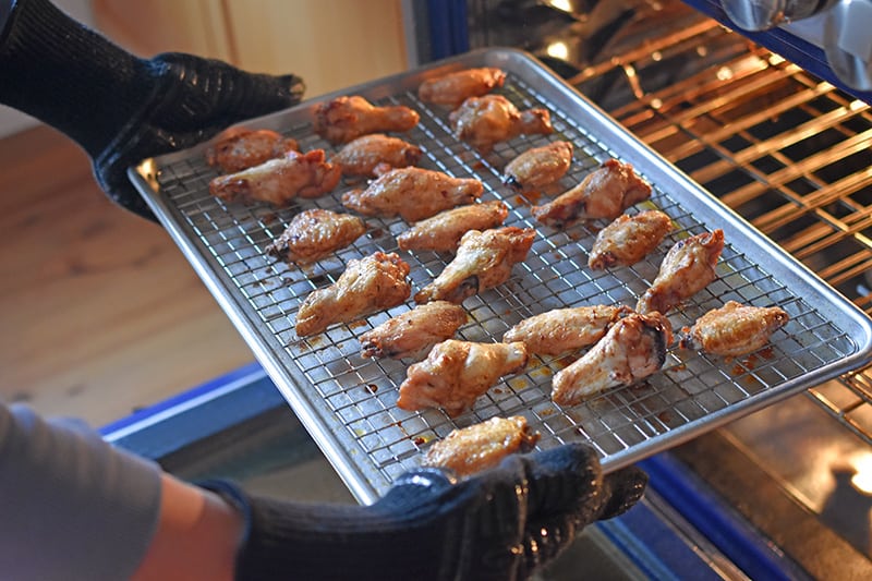 Someone taking out the tray of baked chicken wings magic wings from the oven.