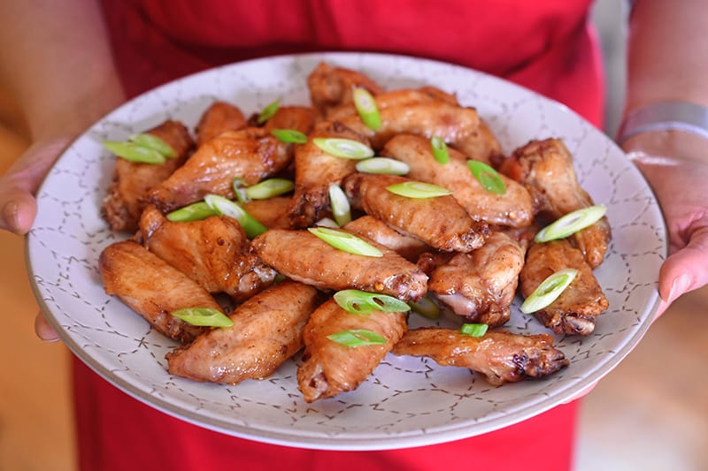 Someone holding a plate of baked chicken wings.