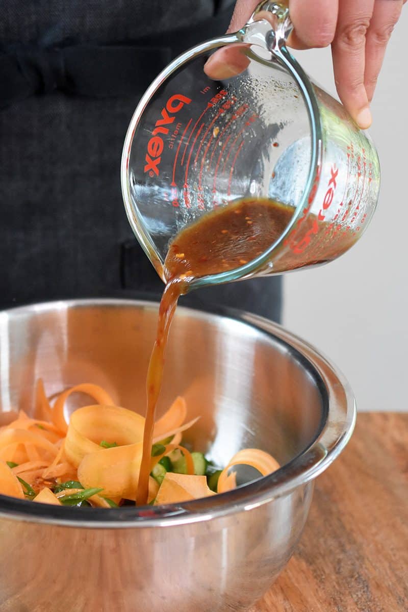 Pour the all-purpose stir-fry dressing into the bowl with the cucumbers, ribboned carrots, and sliced scallions.