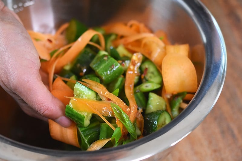 Someone tossing the ingredients for paleo and whole30 smashed cucumber and carrot salad