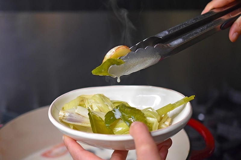 Scooping the lemongrass, galangal, and Makrut lime leaves from the Whole30 Tom Kha Gai broth