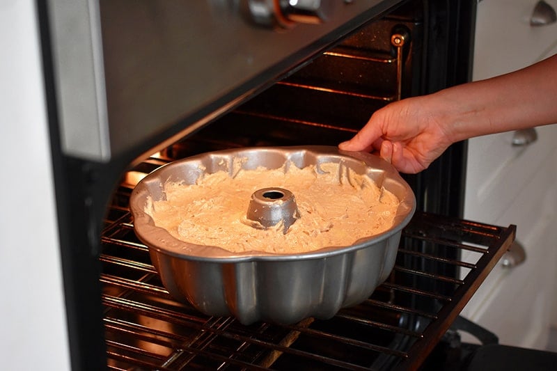 Someone placing a gluten free apple Bundt Cake in the oven.