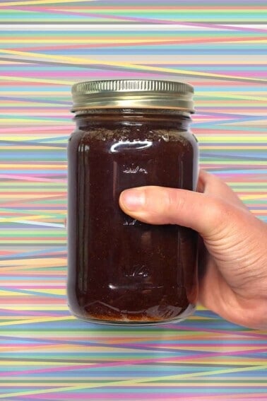 A hand holding a jar of All-Purpose Stir-Fry Sauce in front of a colorful background