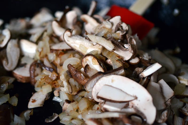 Close-up of onions and mushrooms sautéing in a skillet