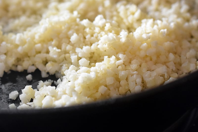 A closeup of cauliflower rice being cooked in a cast iron skillet. 