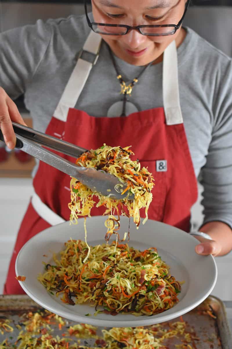 Scooping a plate of Crispy Swoodles with bacon with a pair of tongs.