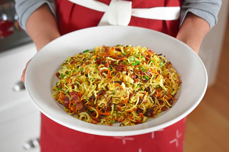 A shot of someone in a red apron holding a large plate of Crispy Swoodles With Bacon.