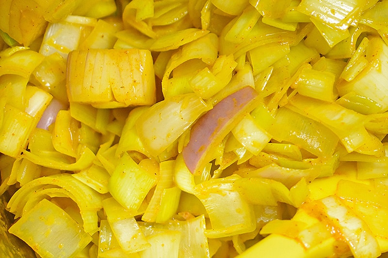 An overhead shot of onions and leeks sautéed with curry powder to make paleo Curried Cream of Broccoli Soup 