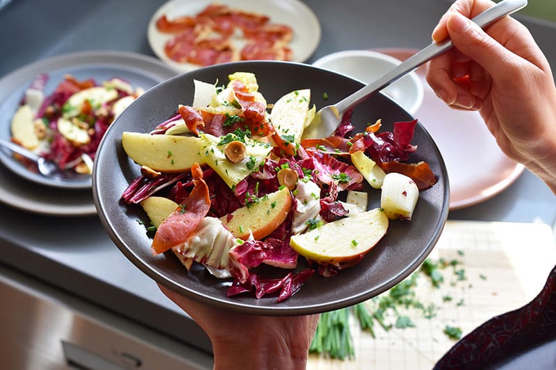 Someone holding a a plate of endive salad, digging into it with a fork.