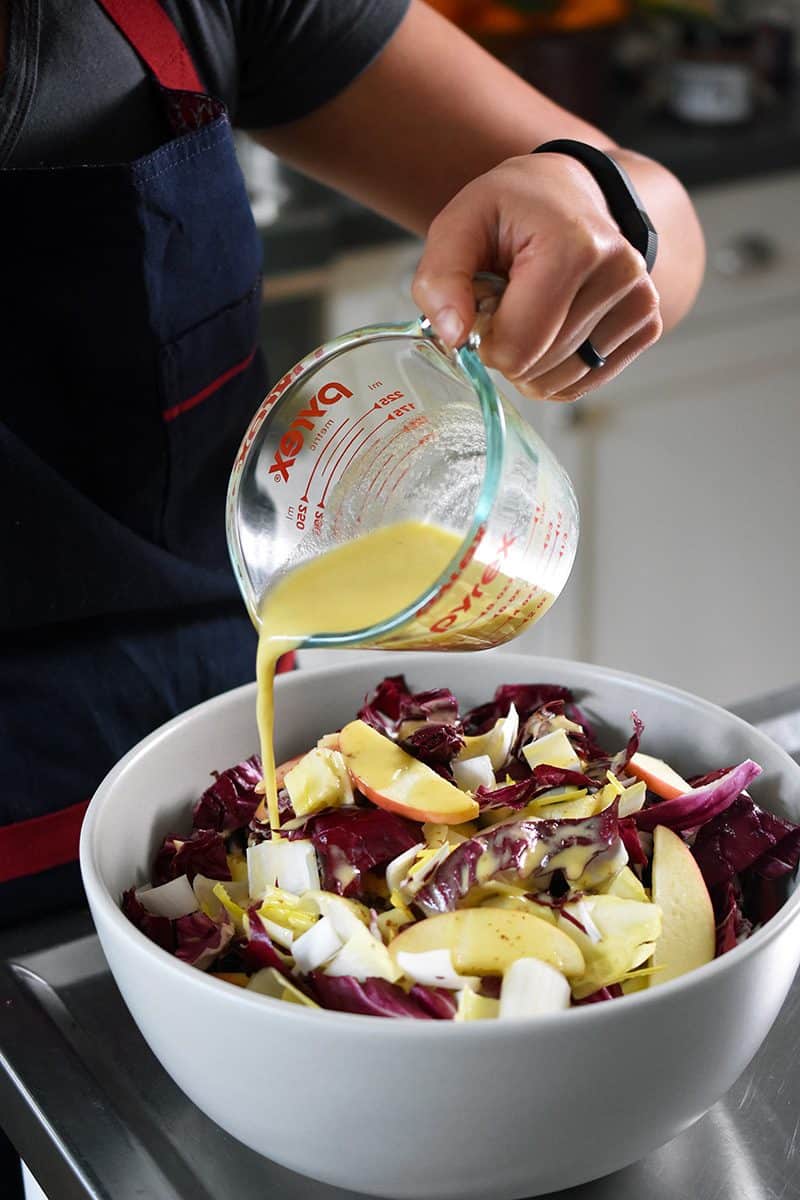 Someone pouring the dressing over the endives and apples in a large bowl.