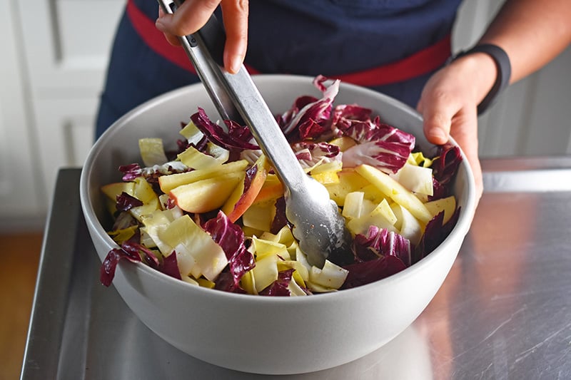 Someone tossing the endive salad with the dressing.