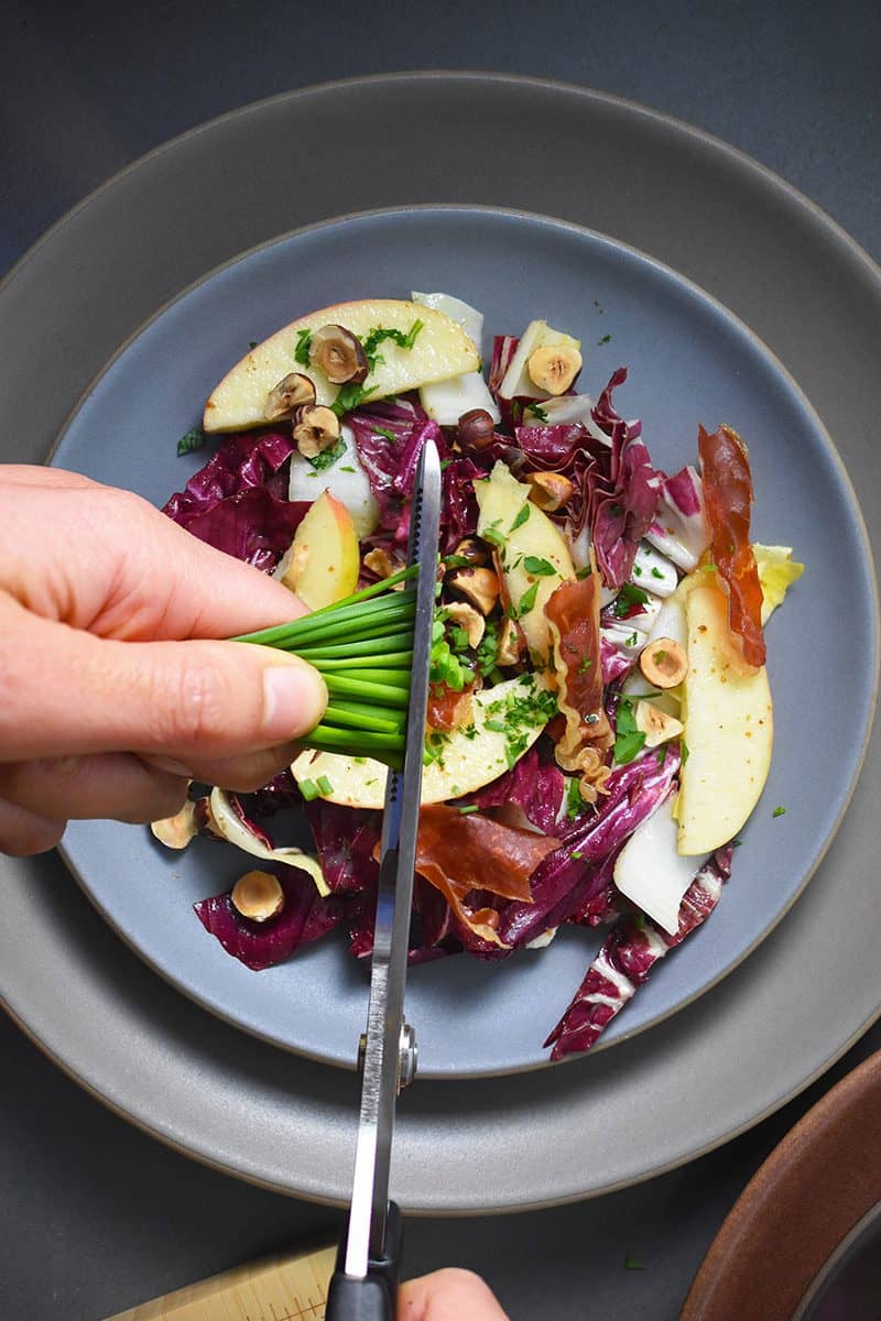 Someone cutting chives over a plate of endive salad.