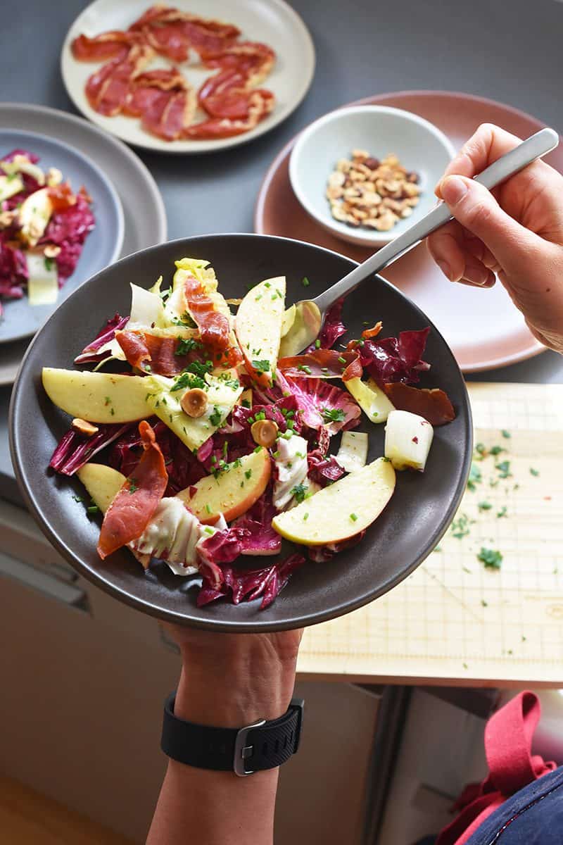 Someone holding a a plate of endive salad, digging into it with a fork.