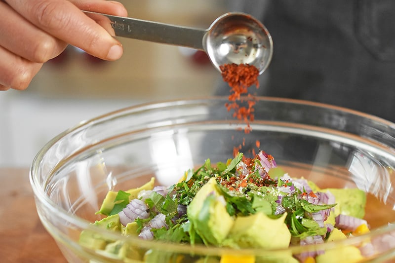 Pouring red pepper flakes into a bowl for the paleo and Whole30 recipe of fried green plantains and mango avocado salsa.