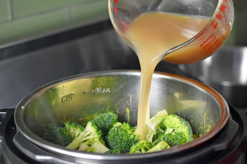 Pouring broth into an Instant Pot to make Curried Cream of Broccoli Soup 