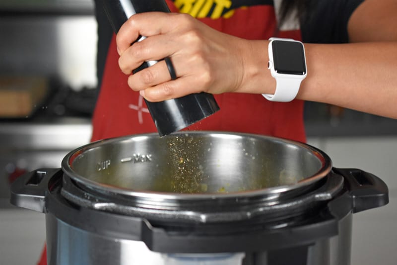 Cracking black pepper into a pot of Instant Pot Curried Cream of Broccoli Soup 