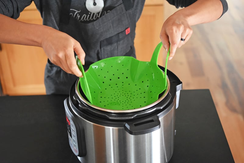 Someone is shown placing a green silicone steamer insert into an Instant Pot.