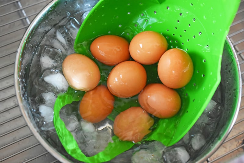 Eight hard cooked eggs are transferred from a silicone steamer to a bowl of ice water.