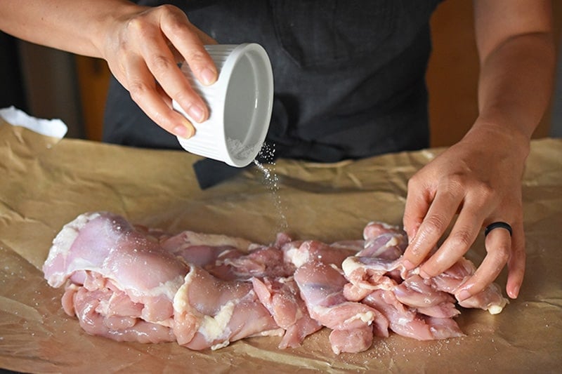 Someone is sprinkling kosher salt on boneless, skinless chicken thighs to make Whole30 Instant Pot Summer Italian Chicken stew