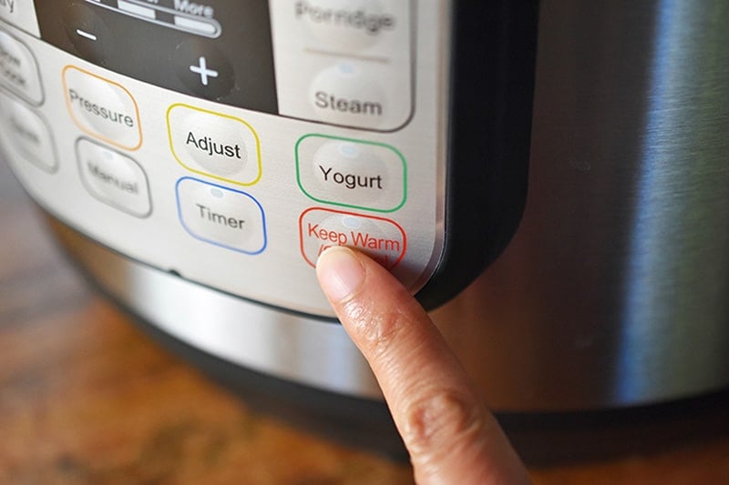 A finer is pressing the Keep Warm/Cancel button on an Instant Pot 