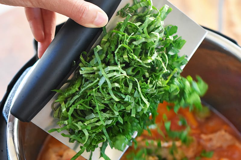 A hand is adding minced fresh herbs to the Instant Pot.