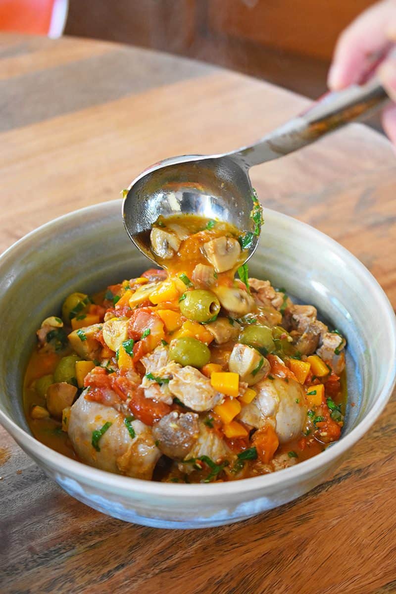 A hand is ladling Instant Pot Summer Italian Chicken into a serving bowl.