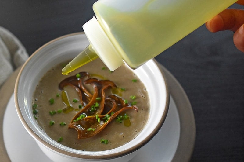 Someone garnishing the cream of mushroom soup with olive oil.