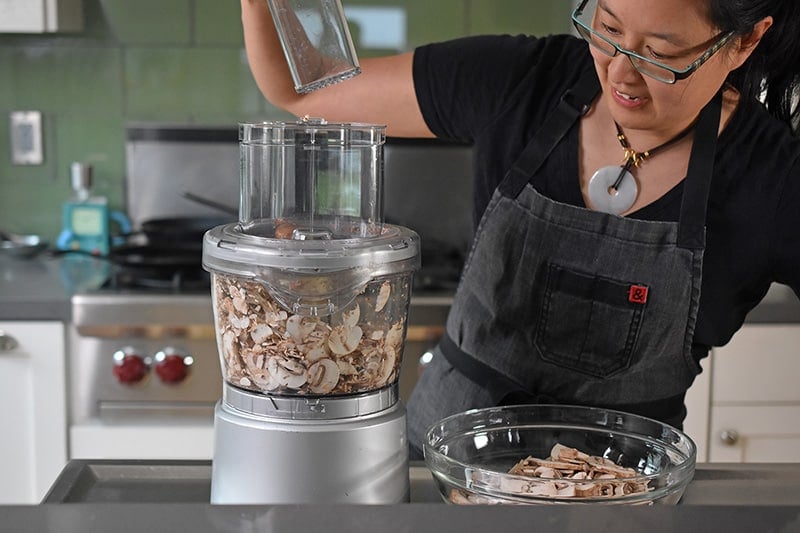 Someone putting mushrooms into a food processor for paleo Instant pot mushroom soup.