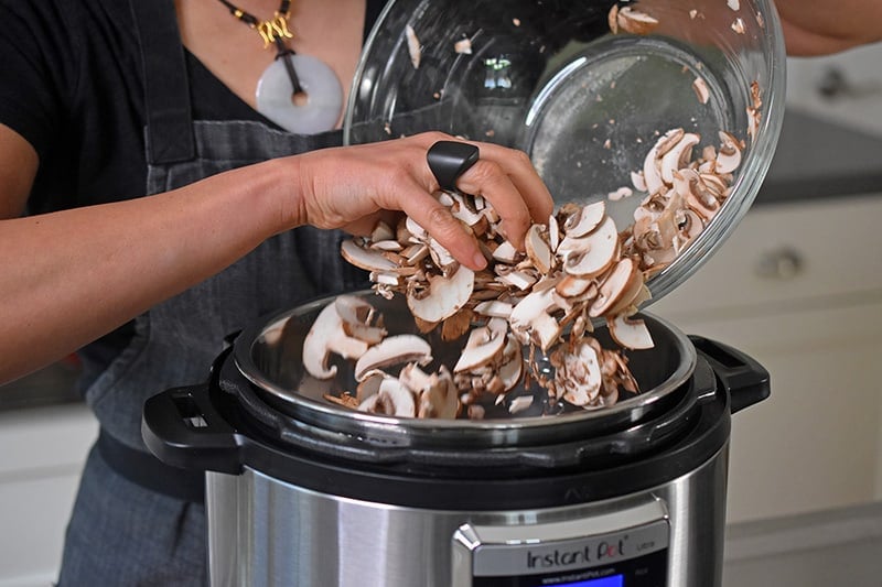 Someone dumping a bowl of chopped mushrooms into an Instant Pot.