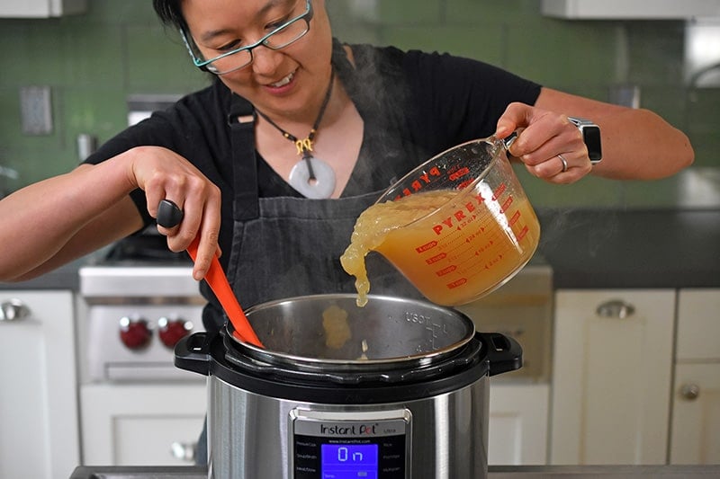 Someone pouring in bone broth into the Instant Pot for Instant Pot cream of mushroom soup.