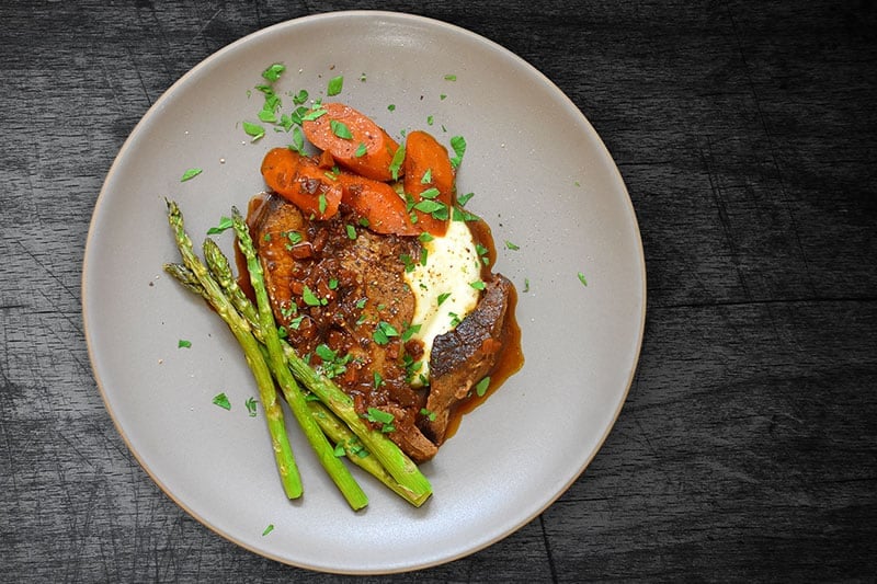 An ovehead shot of a plate of Instant Pot Yankee Pot Roast with roasted asparagus and cauliflower puree