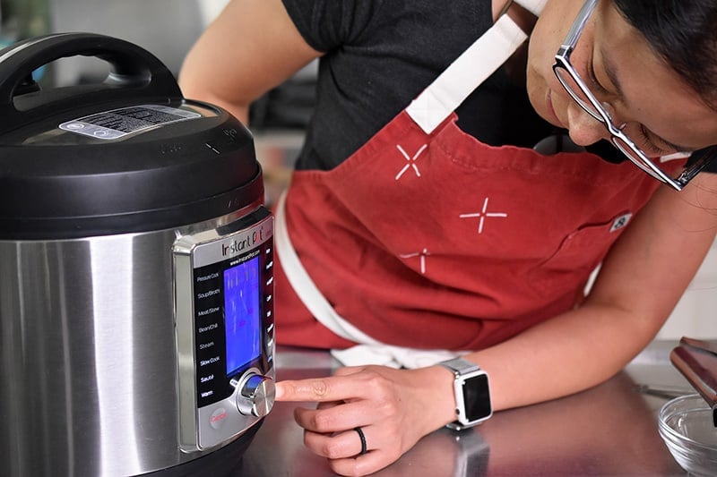 A woman leaning over to program her Instant Pot Ultra.