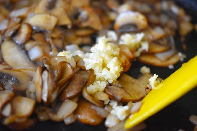 A closeup of minced garlic in the pan with the mushrooms and onions.