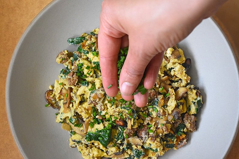 An overhead shot of a hand adding fresh herbs to Joe’s Special Scramble 