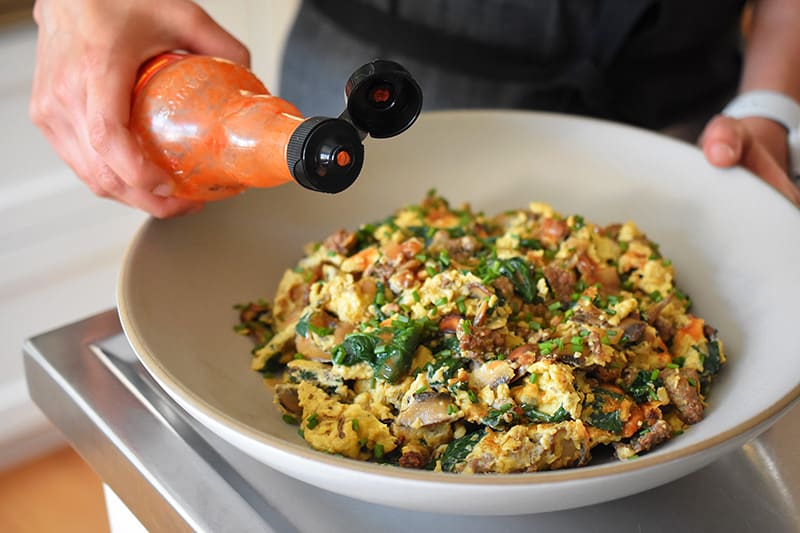 Someone adds hot sauce to a plate of Joe’s Special Scramble.