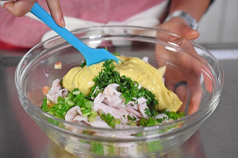 Someone mixing together ingredients for curry chicken salad.