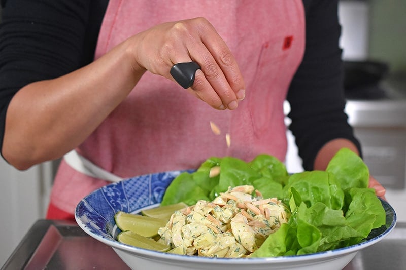 Someone sprinkling toasted almonds on a bowl of madras curry chicken salad.