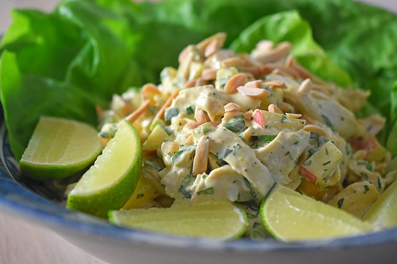 Curry chicken salad in a bowl with limes and butter lettuce.