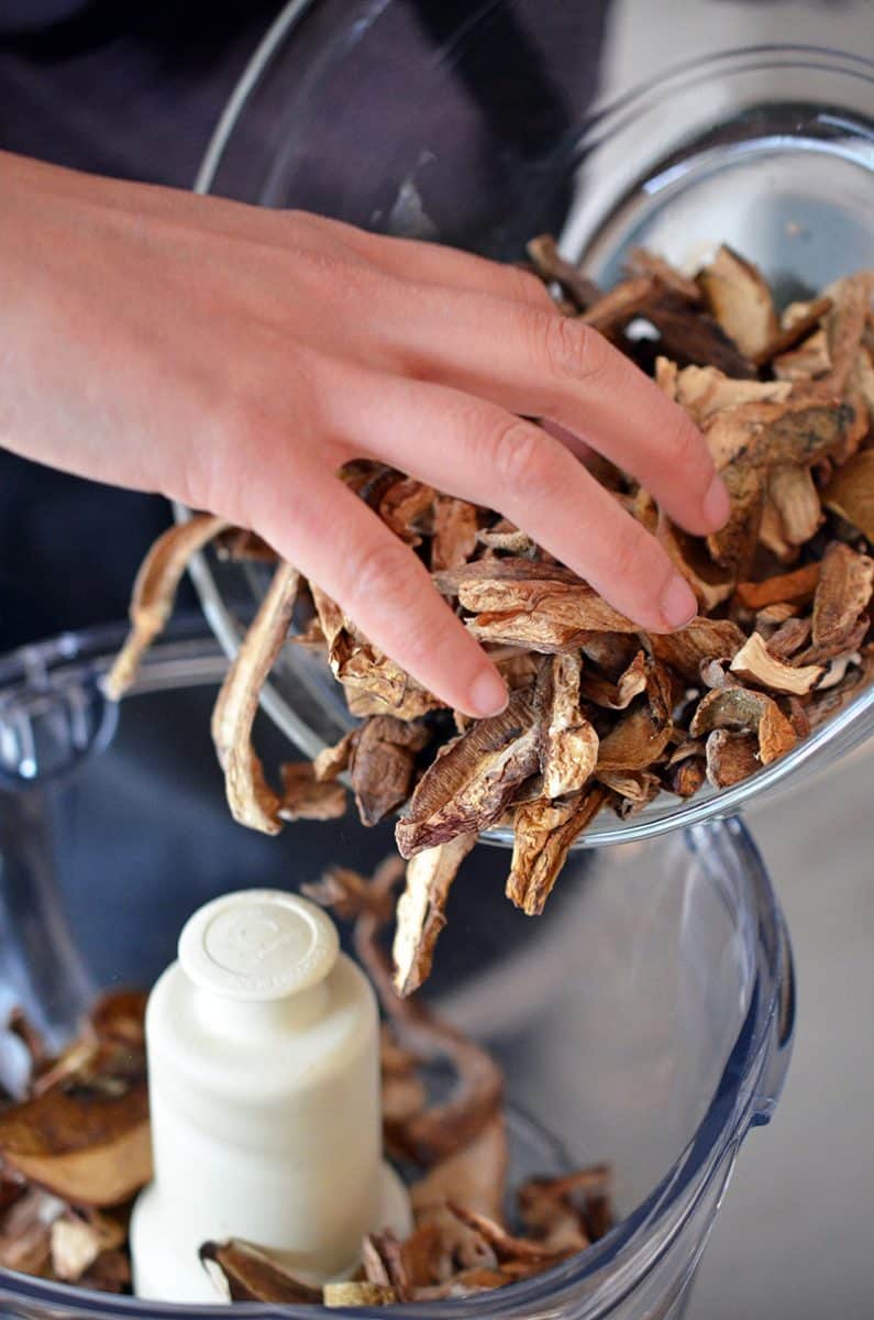 Adding a bow of dried porcini mushrooms to a food processor 