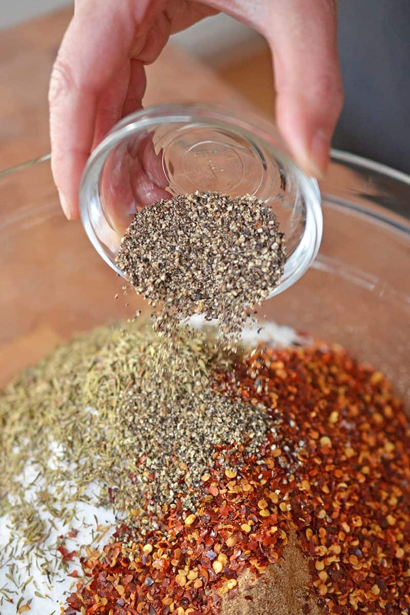 Adding freshly ground black pepper to the bowl of Magic Mushroom Powder ingredients